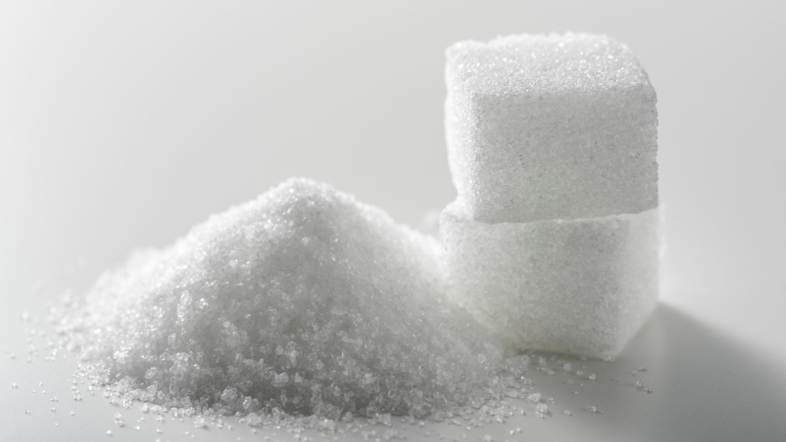 White sugar crystals and sugar cubes on a light surface